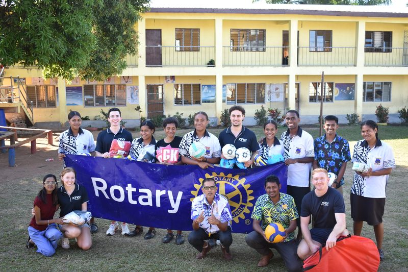 KFK volunteers and students behind a Rotary banner, holding donated balls outside a Fijian school