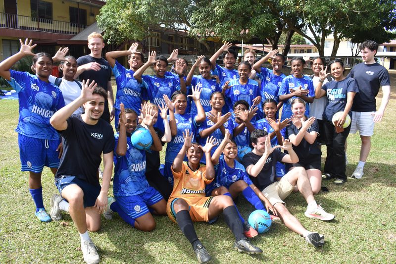 A girls' football team and KFK volunteers celebrating with hands raised