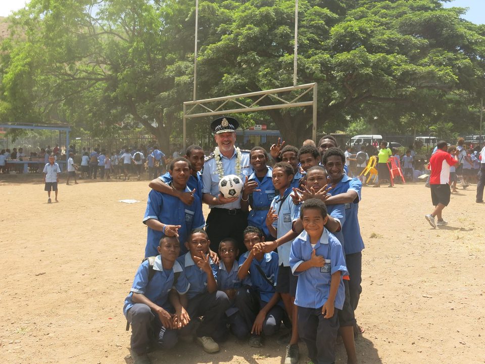 An Australian Federal Police officer surrounded by smiling school children holding a soccer ball in Papua New Guinea